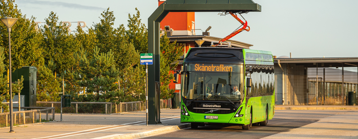 En grönfärgad elbuss står och laddar vid en laddningsstation. 